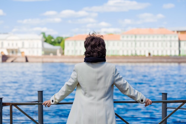 Beautiful young woman walks along embankment in white coat and black sweatshirt