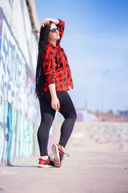 A beautiful young woman walks around the city in a plaid shirt and with African braids African hairstyle afro braids trendy trend freak modern hairstyle