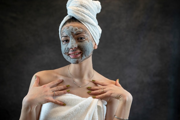 Beautiful young woman wear white towel applying gray oxygen bubbling mask isolated on black