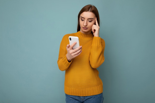 Beautiful young woman wearing casual clothes standing isolated over background surfing on the internet via phone looking at mobile screen.