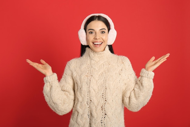 Beautiful young woman wearing earmuffs on red background