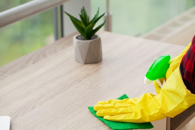 Beautiful young woman wearing protective gloves cleaning the desk in office