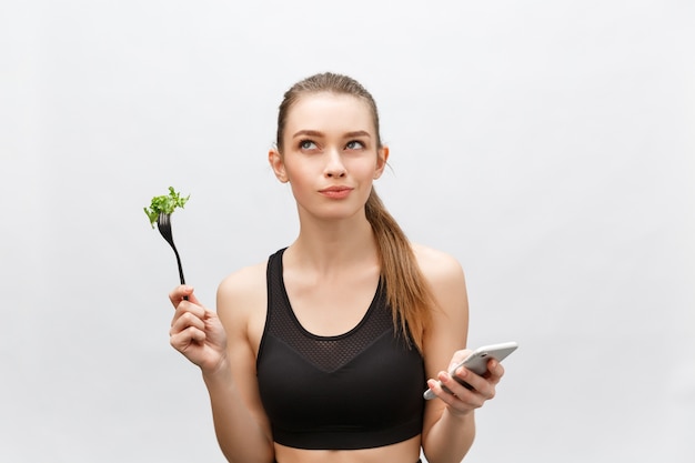 Photo beautiful young woman wearing sport clothes with salad in hand, using smart phone.