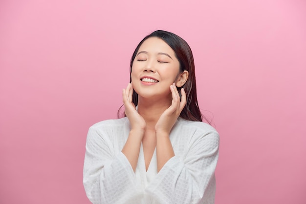 Beautiful young woman wearing white bathrobes is touching her face and smiling