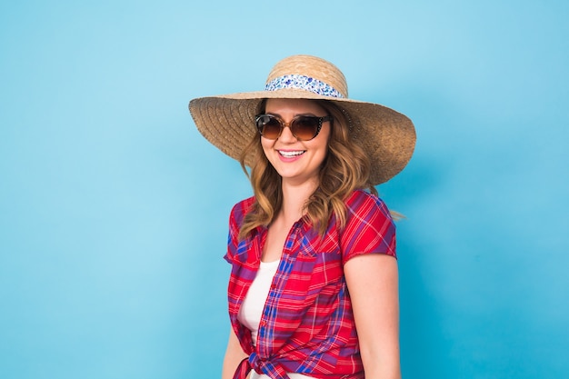 Beautiful young woman wears in summer dress and straw hat is laughing on blue background with copy space.