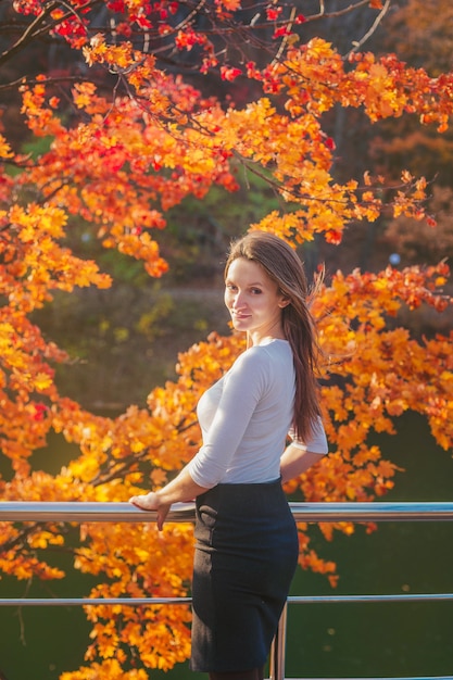 Beautiful young woman in a white blouse in the park in autumn. Portrait of a woman in the park with a lake and trees.