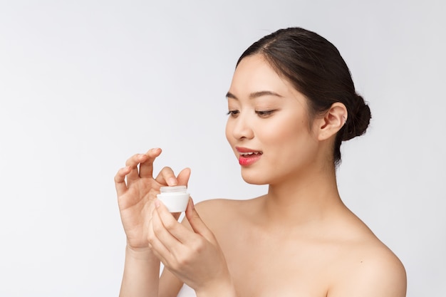 Beautiful young woman on white isolated wall holding cosmetic face cream, asian