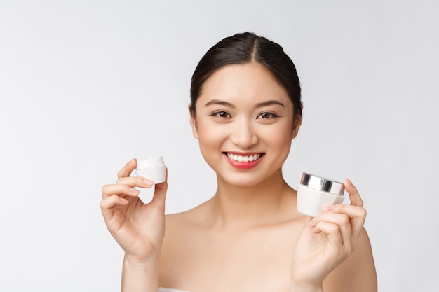 Beautiful young woman on white isolated wall holding cosmetic face cream, asian