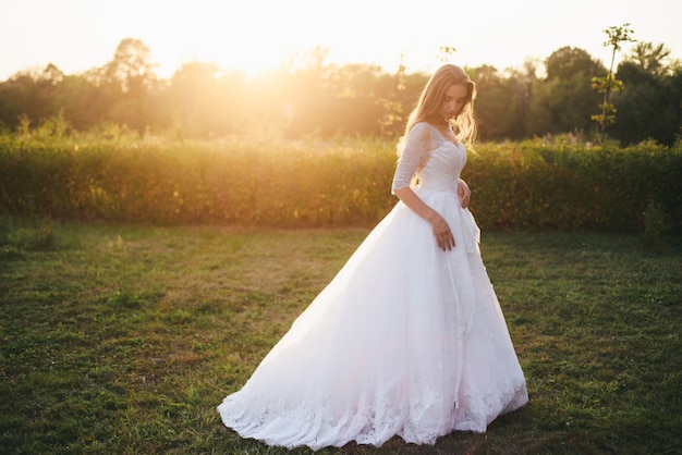 Beautiful young woman in a white wedding dress and black boots at sunset.