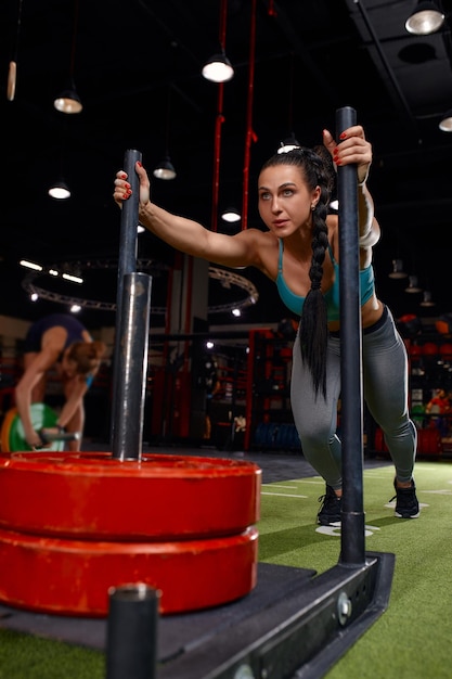 Beautiful young woman with barbell weight plate working out in sports club