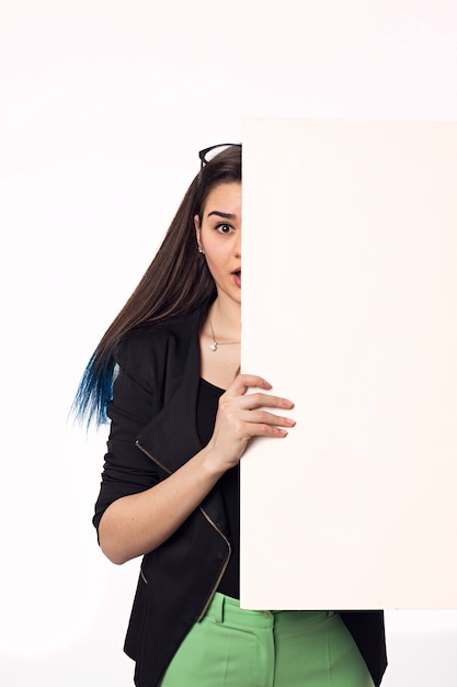 Beautiful young woman with big empty poster on the white wall