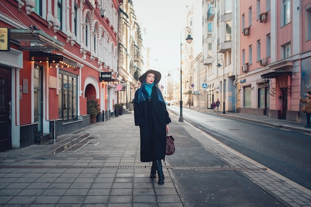 Beautiful young woman with blue hair in nice black coat, jeans and hat.