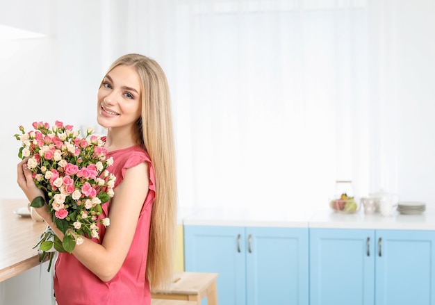 Beautiful young woman with bouquet of roses at home