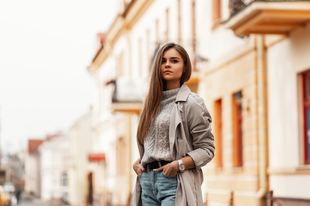 Beautiful young woman with brown long hair in a stylish trench coat posing in the city outdoors