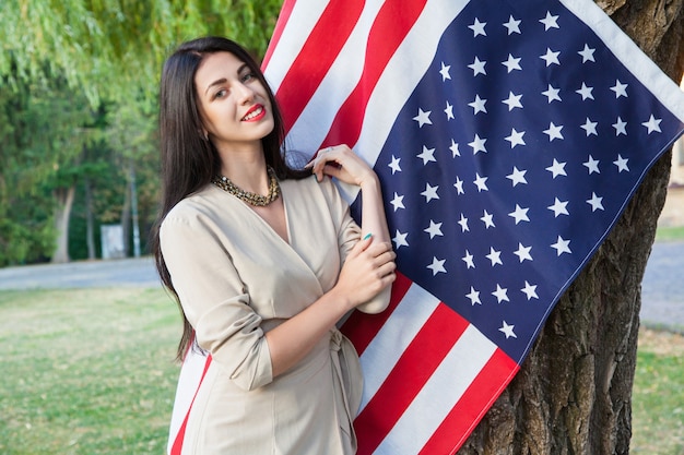 Beautiful young woman with classic dress near american flag in the park fashion model holding us