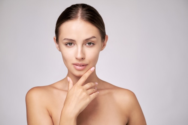 Beautiful young woman with clean fresh skin standing over light grey background