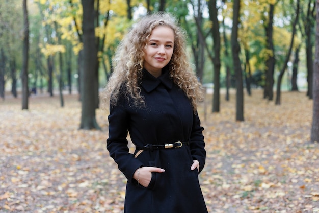 Beautiful young woman with curly hair, green eyes. girl in casual clothes relaxing in park in good autumn weather, covered with fallen leaves.