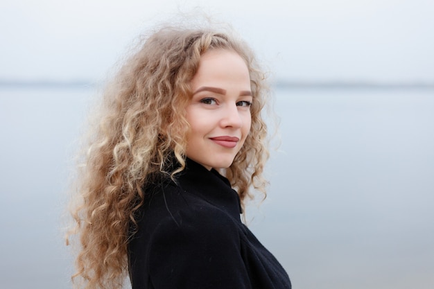 Beautiful young woman with curly hair, green eyes. girl in casual clothes relaxing in park in good autumn weather, covered with fallen leaves.