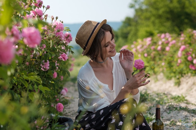 Beautiful young woman with curly hair posing near roses in a garden. The concept of perfume advertising.