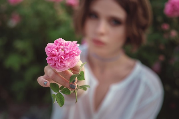 Beautiful young woman with curly hair posing near roses in a garden The concept of perfume advertising