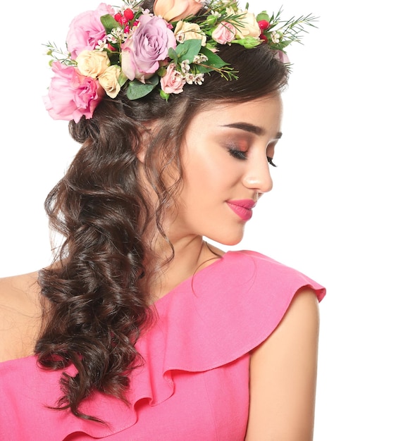 Beautiful young woman with flower wreath on white background