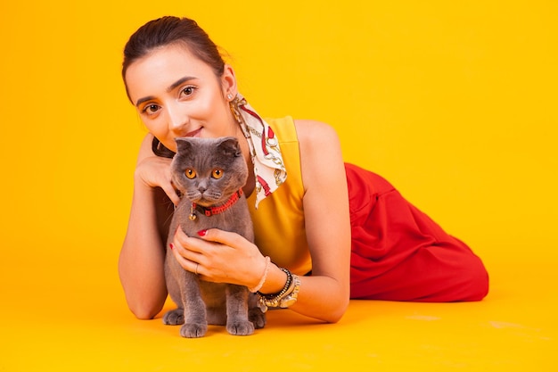 Photo beautiful young woman with his adorable cat in studio over yellow background.