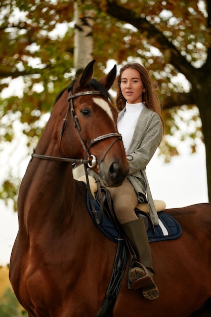 Beautiful young woman with horse outdoor Concept of animal care Rural rest and leisure Idea of green tourism Young european woman wearing helmet and uniform