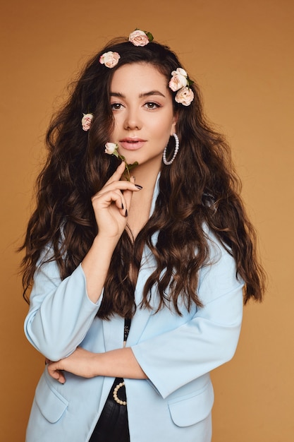 Beautiful young woman with long curly hair decorated with rose flowers