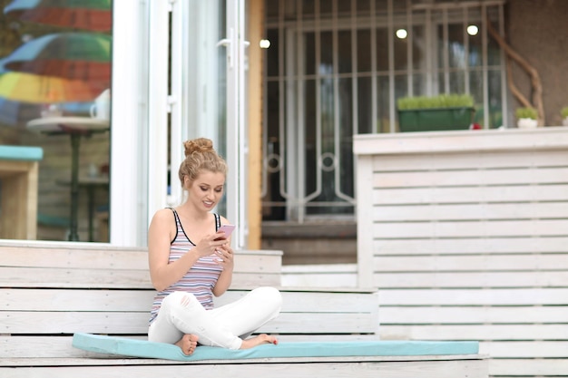 Beautiful young woman with mobile phone sitting on stairs outdoors