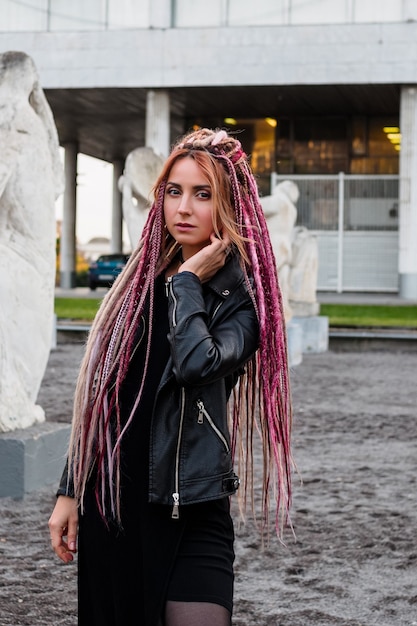 Beautiful young woman with pink long dreadlocks in black dress and leather jacket