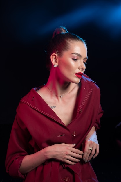 Beautiful young woman with red lips and high tail in Burgundy cloak on black.