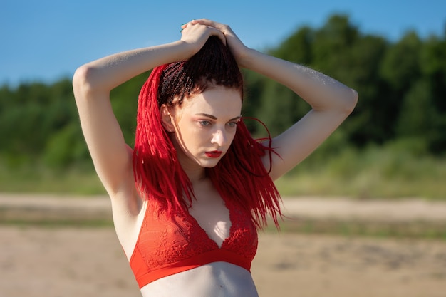 Beautiful young woman with scarlet dreadlocks and red bathing suit enjoying nature.