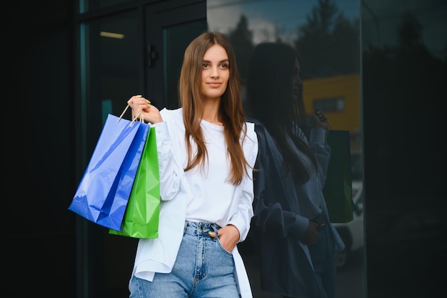 Beautiful young woman with shopping bags near shop outdoors