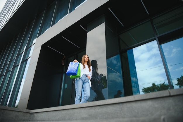 Beautiful young woman with shopping bags near shop outdoors