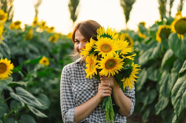 Beautiful young woman with sunflowers enjoying nature and laughing on summer sunflower field