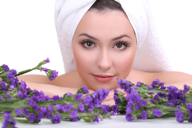 Beautiful young woman with towel on her head and flowers isolated on white