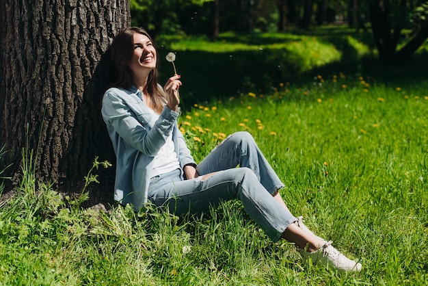 Beautiful young woman with white dandelion in park