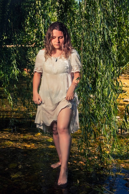 Beautiful young woman with white dress near stream of water.