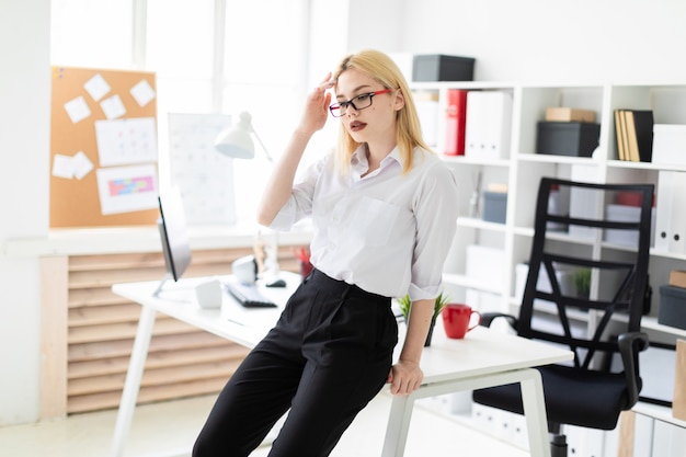 Beautiful young woman working in a bright office at a computer Desk. The woman has white hair and wearing glasses.