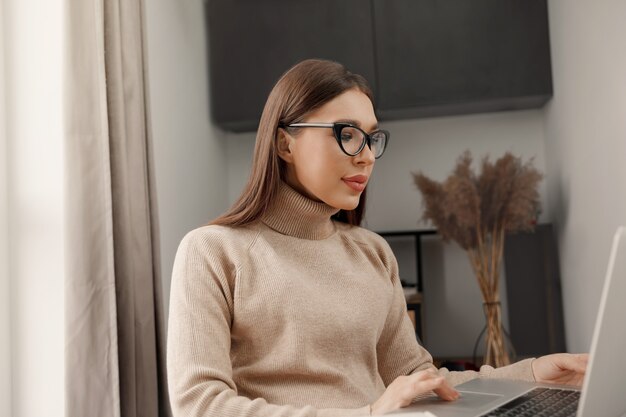 Beautiful young woman working on laptop computer while sitting at the living room drinking coffee  Communicates on internet Remote work Elearning concept