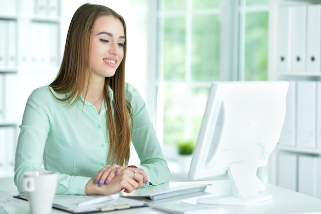 Beautiful young woman working at table with computer in office