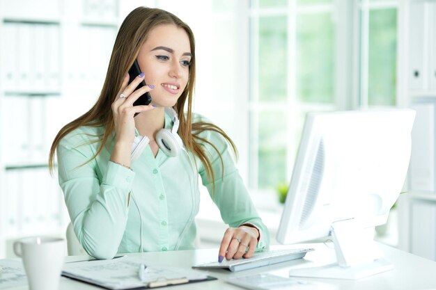 Beautiful young woman working with computer while talking on phone