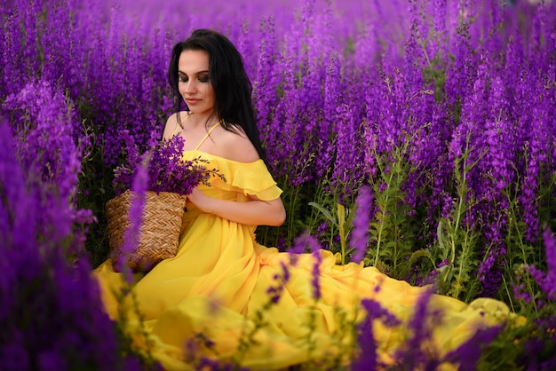 Beautiful young woman in a yellow dress sits in a field of purple flowers.