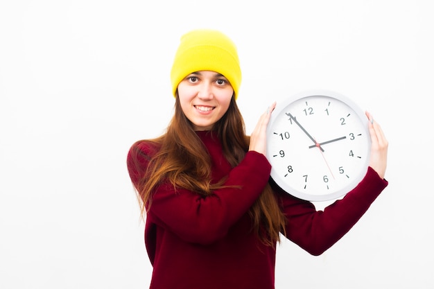 Beautiful young woman in a yellow hat holds a clock in her hands smiling and looking at the frame