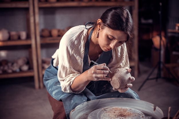 Photo beautifulyoung woman master demonstrates the process of making ceramic dishes using the old technology. folk handicraft.