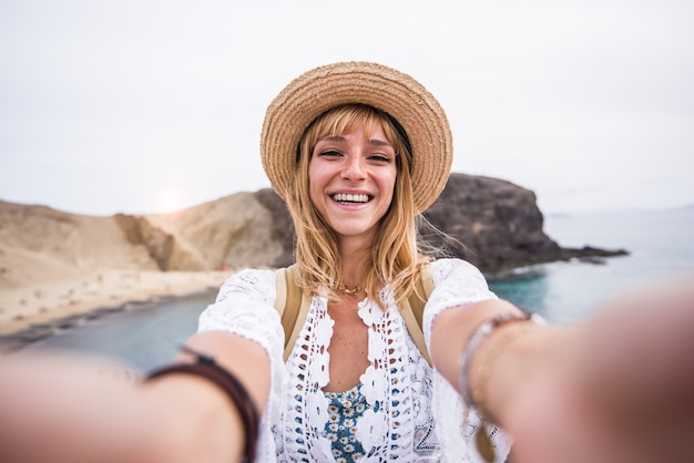 Beautiul young woman with hat taking a selfie at the beach.