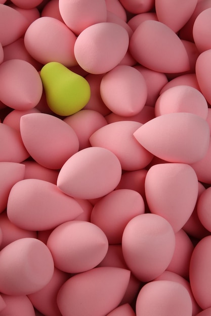 Beauty background a bunch of pink gentle sponges and one contrast green conflict for makeup vertical