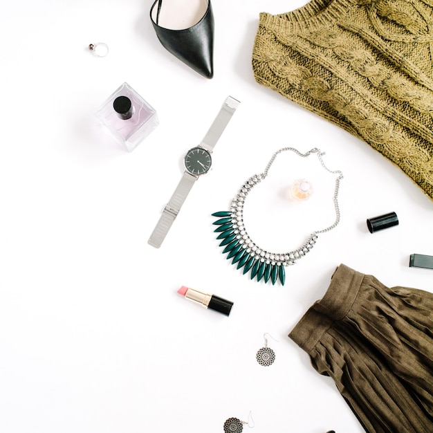 Beauty blog concept. Female clothes and accessories: green skirt and sweater, watches, necklace, lipstick, shoes, sunglasses on white background. Flat lay, top view trendy fashion feminine background.