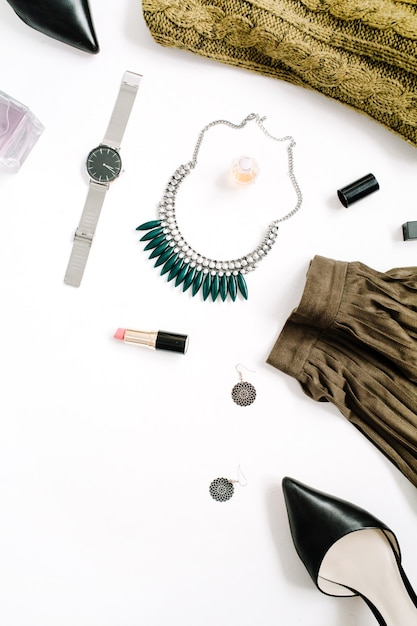 Beauty blog concept. Female clothes and accessories: green skirt and sweater, watches, necklace, lipstick, shoes, sunglasses on white background. Flat lay, top view trendy fashion feminine background.