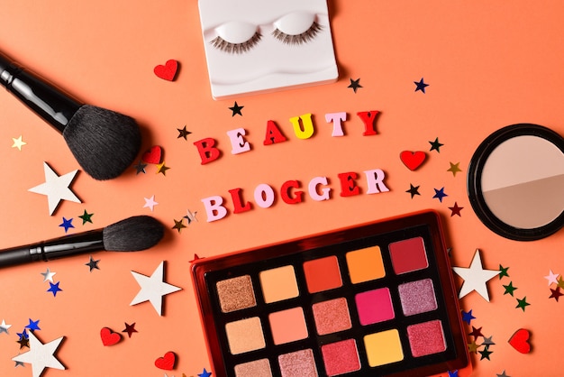 Beauty blogger text on an orange background. Professional trendy makeup products with cosmetic beauty products,  eye shadows, eye lashes, brushes and tools.